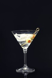 Martini cocktail with ice and olives on dark background