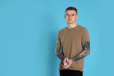 Photo of Young man with tattoos on light blue background. Space for text