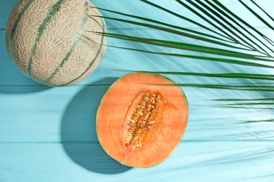 Photo of Tasty ripe cantaloupe melons and palm leaf on light blue wooden table, flat lay