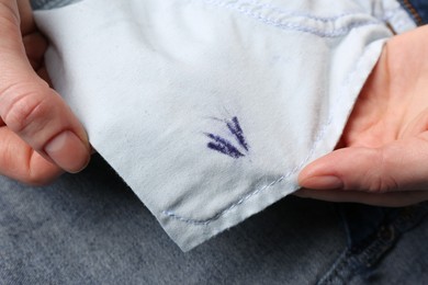 Photo of Woman holding jeans with ink stain, closeup