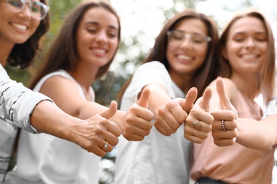Photo of Happy women showing thumbs up outdoors, focus of hands. Girl power concept