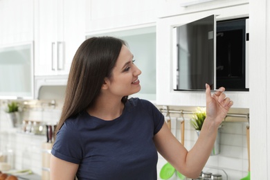 Young woman opening modern microwave oven in kitchen