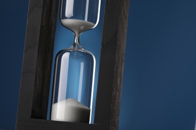 Photo of Hourglass with flowing sand on blue background, closeup. Space for text