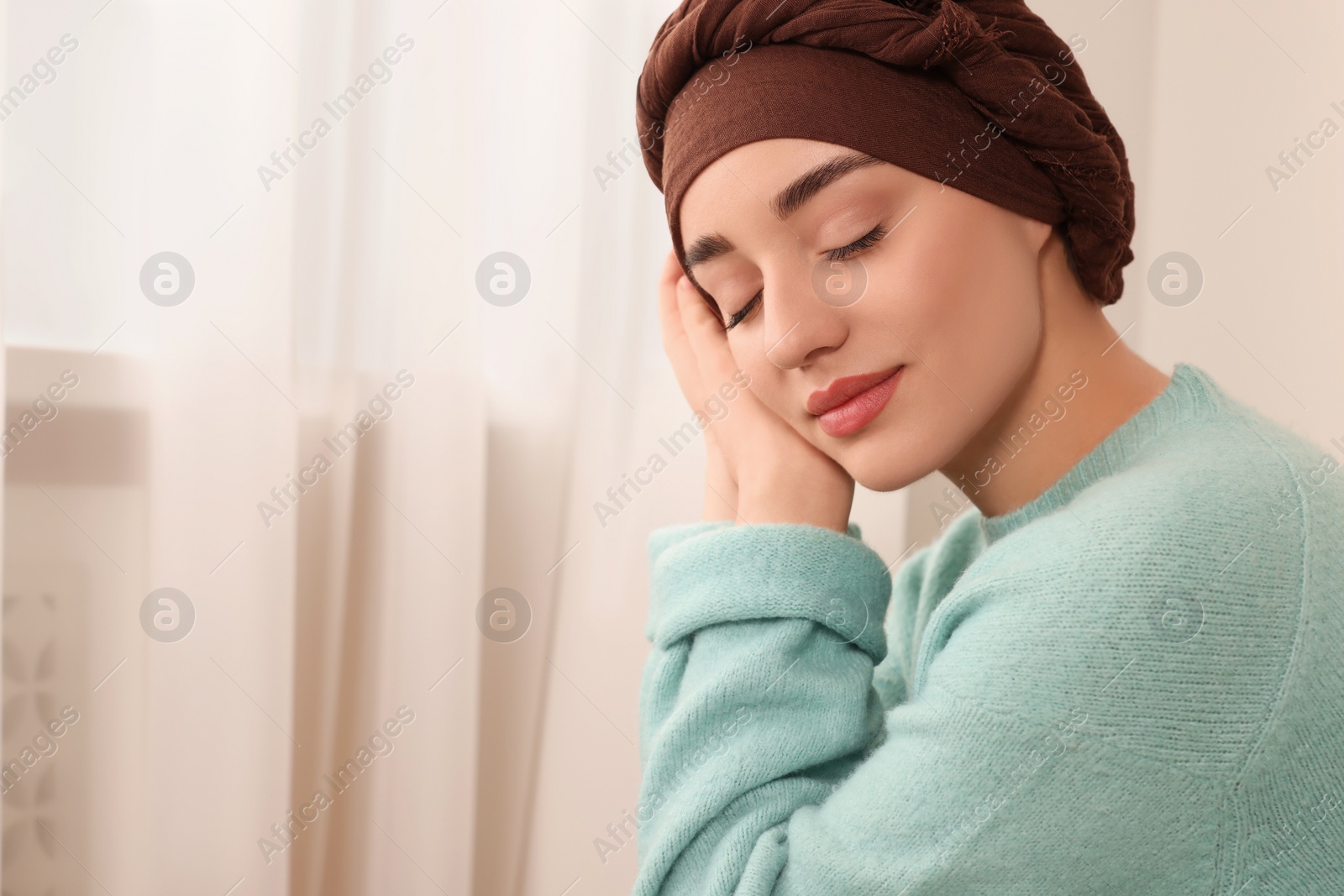 Photo of Cancer patient. Young woman with headscarf near window indoors, space for text