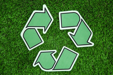 Photo of Paper recycling symbol on green grass, top view