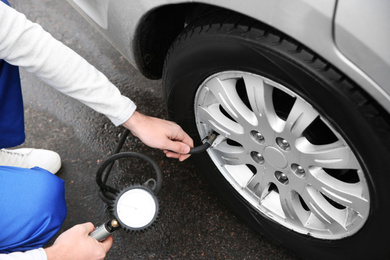 Photo of Mechanic checking tire pressure in car wheel at service station, closeup