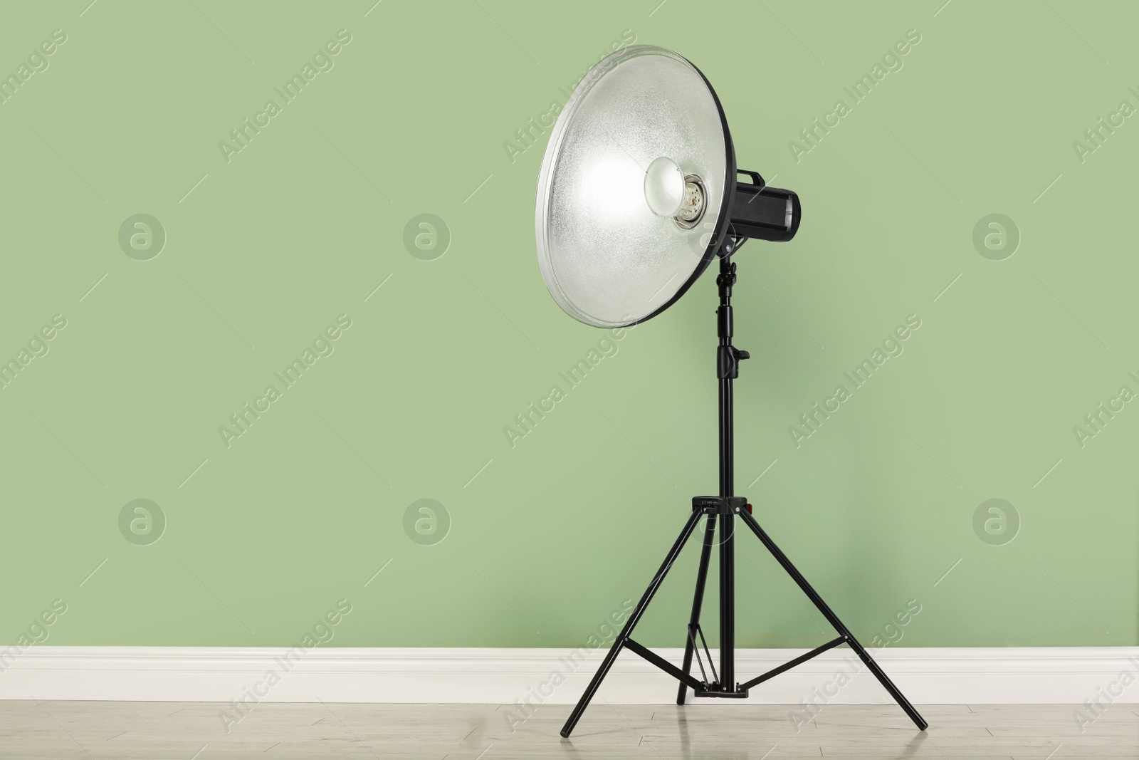 Photo of Professional beauty dish reflector on tripod near pale green wall in room, space for text. Photography equipment