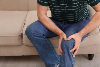 Photo of Senior man suffering from knee pain at home, closeup