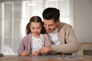 Photo of Man and his little daughter playing with puzzles at home