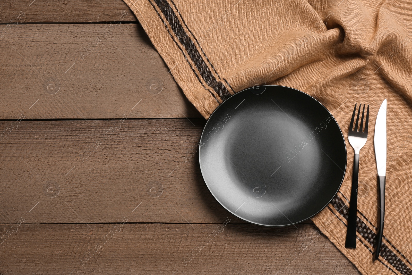 Photo of Clean plate and shiny silver cutlery on wooden table, flat lay. Space for text