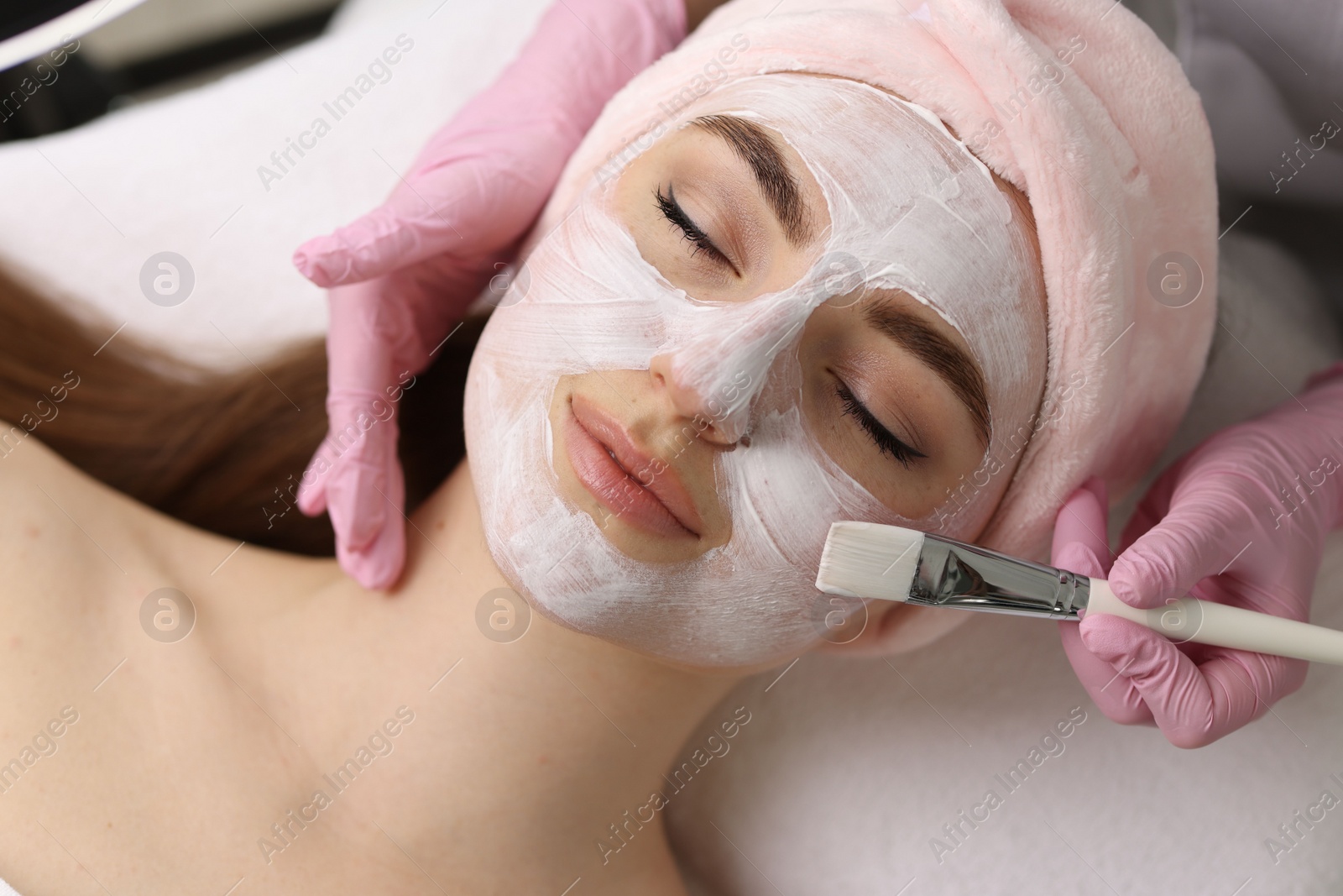 Photo of Cosmetologist applying mask on woman's face, top view