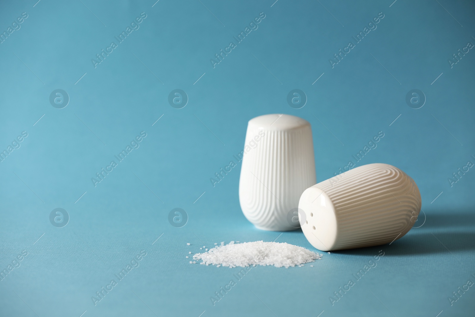 Photo of Organic salt and shakers on light blue background. Space for text