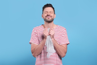 Photo of Man popping bubble wrap on light blue background. Stress relief