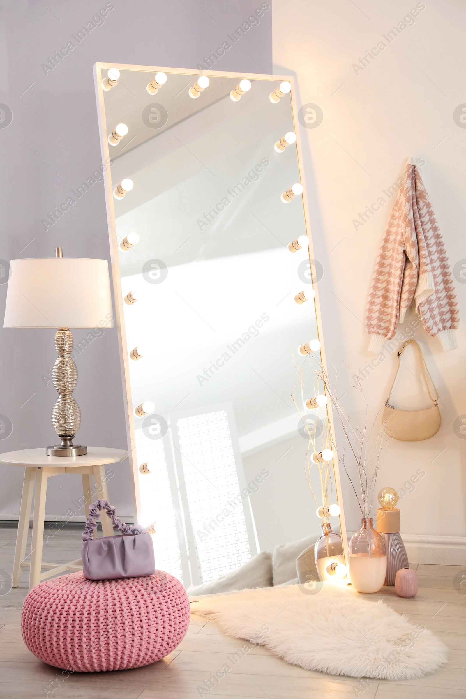 Photo of Large mirror with light bulbs and knitted pouf in stylish room. Interior design