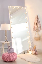 Large mirror with light bulbs and knitted pouf in stylish room. Interior design