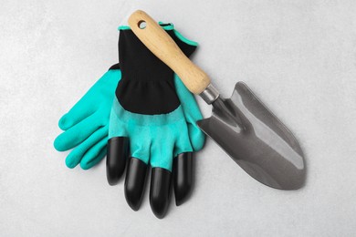 Photo of Pair of claw gardening gloves and trowel on light grey table, top view