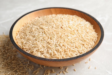 Photo of Bowl with raw unpolished rice on light background