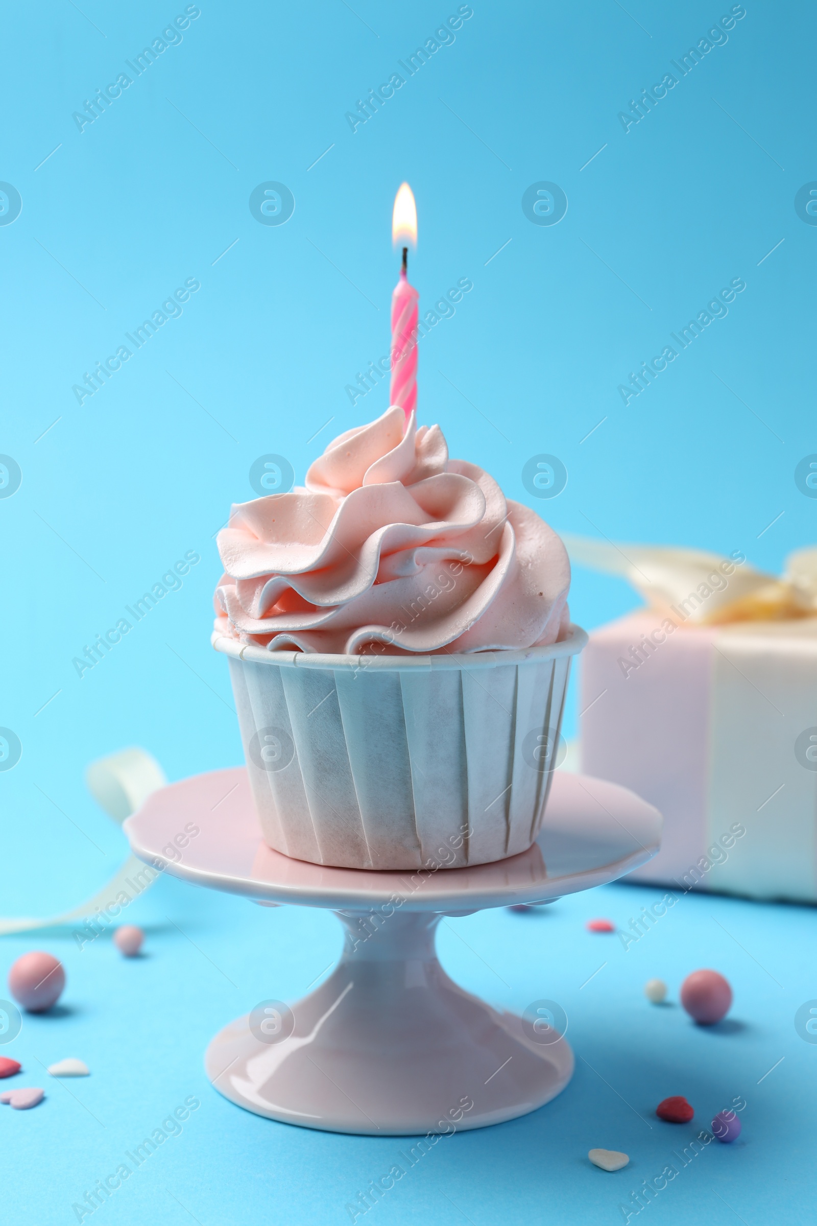 Photo of Delicious birthday cupcake with burning candle and sprinkles on light blue background, closeup