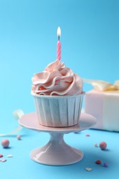 Delicious birthday cupcake with burning candle and sprinkles on light blue background, closeup