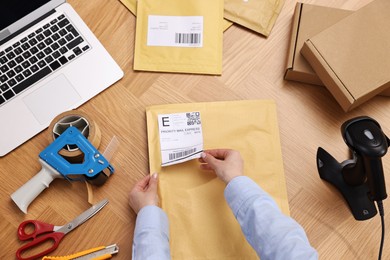 Photo of Parcel packing. Post office worker sticking barcode on bag at wooden table, top view