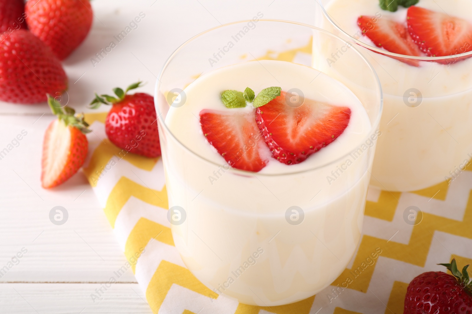 Photo of Tasty yogurt and strawberries in glasses on white wooden table, closeup