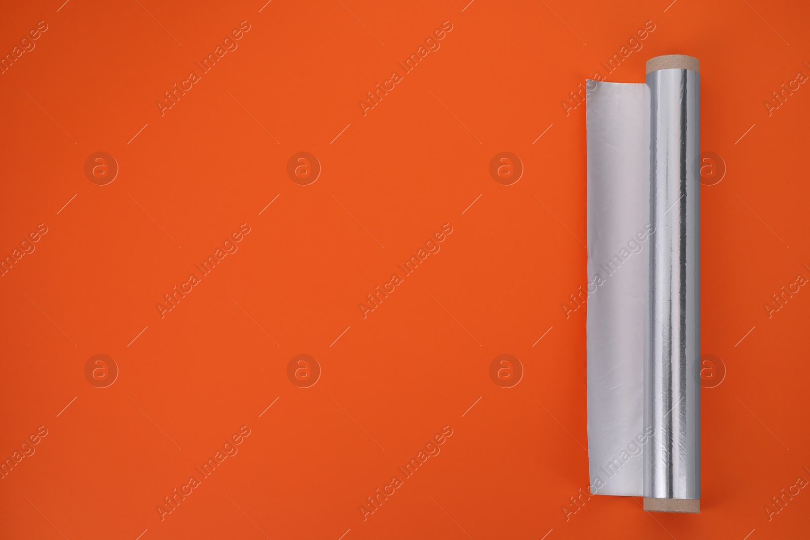 Photo of Roll of aluminum foil on orange background, top view. Space for text