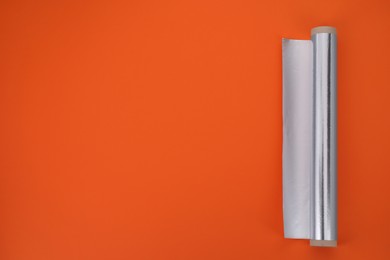 Photo of Roll of aluminum foil on orange background, top view. Space for text