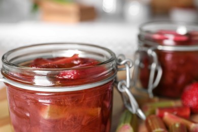 Tasty rhubarb jam in jar on blurred background, closeup