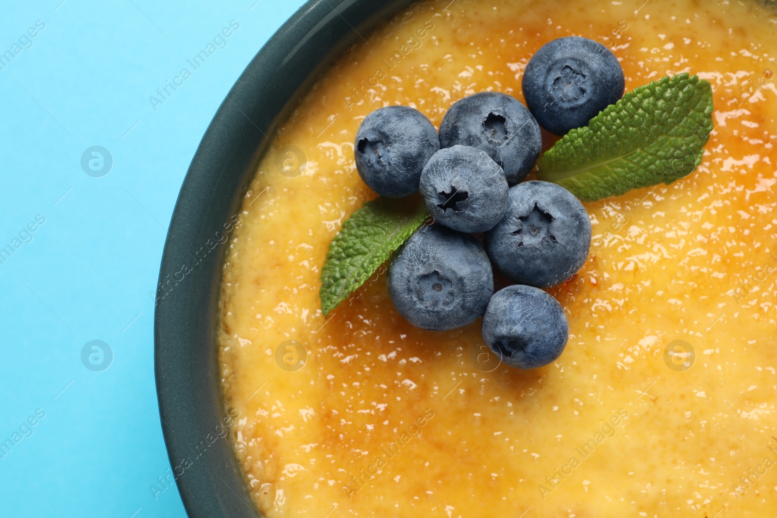 Photo of Delicious creme brulee with fresh blueberries and mint on light blue background, top view