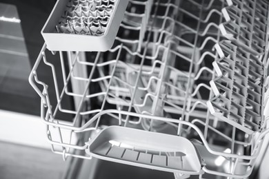 Photo of Open clean empty dishwasher in kitchen, closeup