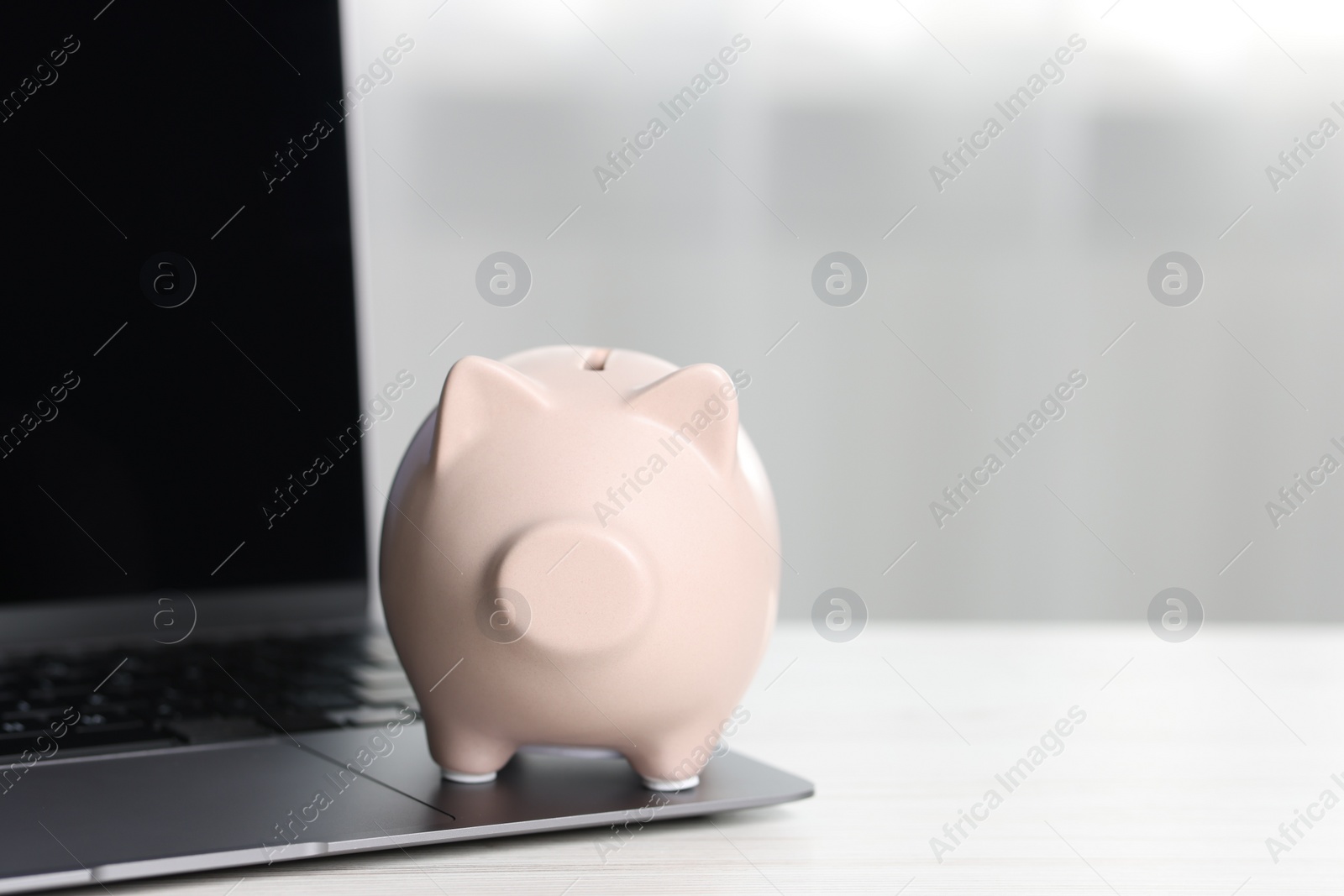 Photo of Piggy bank and laptop on white table indoors. Space for text