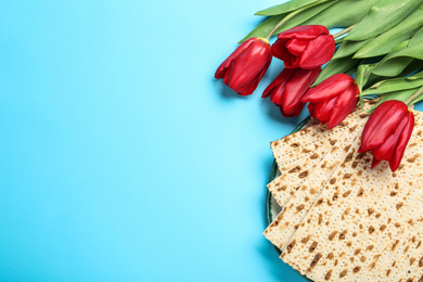 Photo of Matzos and flowers on light blue background, flat lay with space for text. Passover (Pesach) Seder