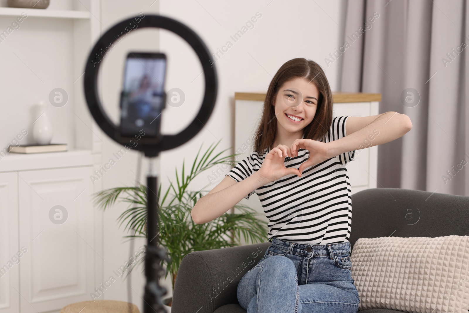 Photo of Smiling teenage blogger making heart gesture to her subscribers while streaming at home