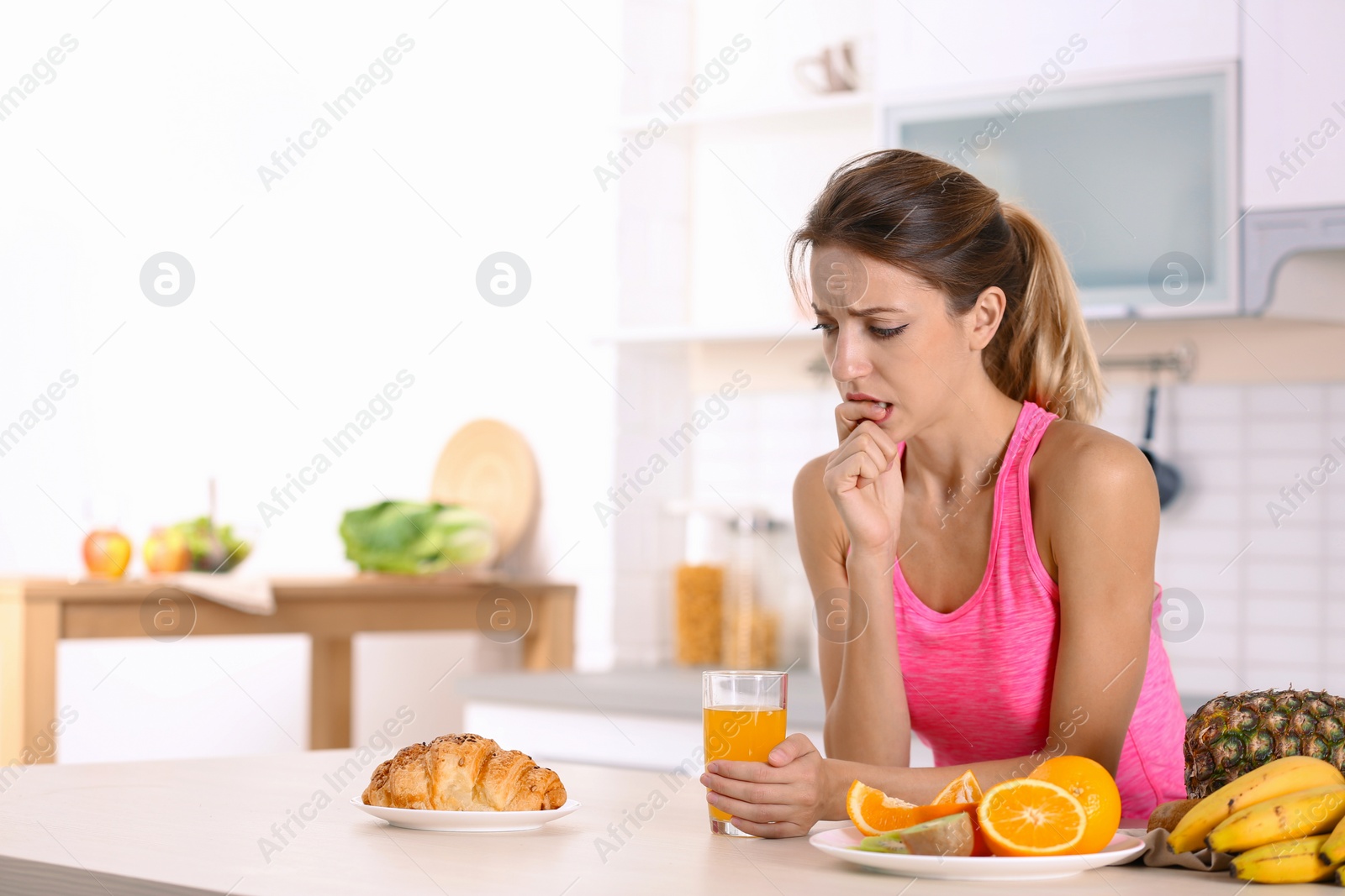 Photo of Woman choosing between dessert and fruits at table in kitchen. Healthy diet