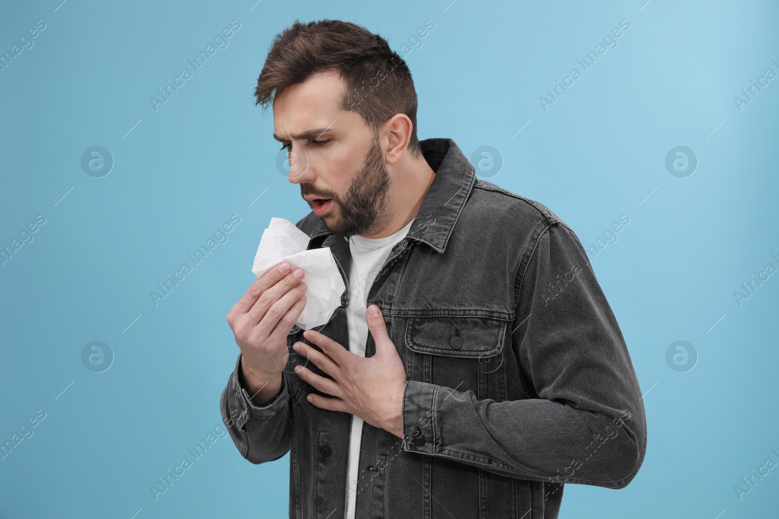 Photo of Man coughing on light blue background. Cold symptoms