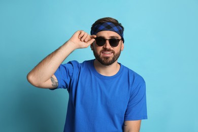 Photo of Fashionable young man in stylish outfit with bandana on light blue background