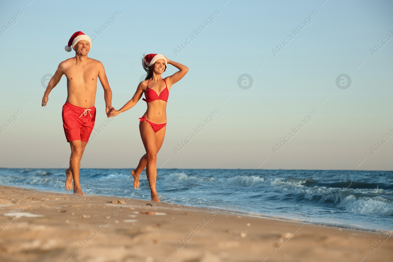 Photo of Happy couple with Santa hats together on beach. Christmas vacation