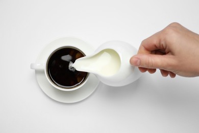 Woman pouring milk into cup of coffee on white background, top view
