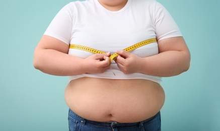 Photo of Overweight woman with measuring tape on color background