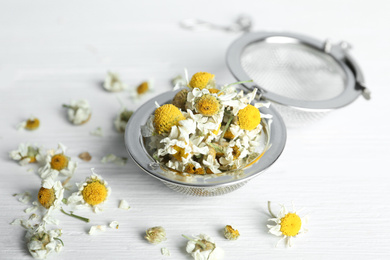 Photo of Dry chamomile flowers in infuser on white wooden table, closeup