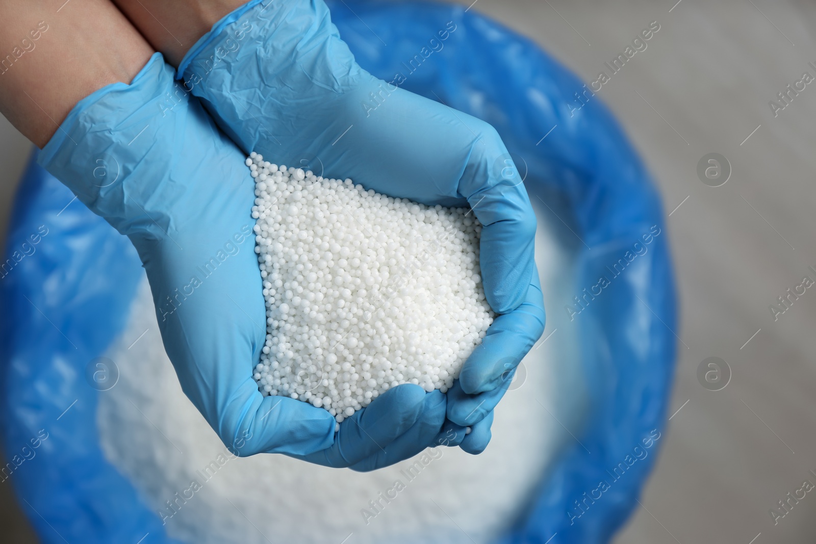 Photo of Person in gloves holding pile of ammonium nitrate pellets over bag, top view. Mineral fertilizer