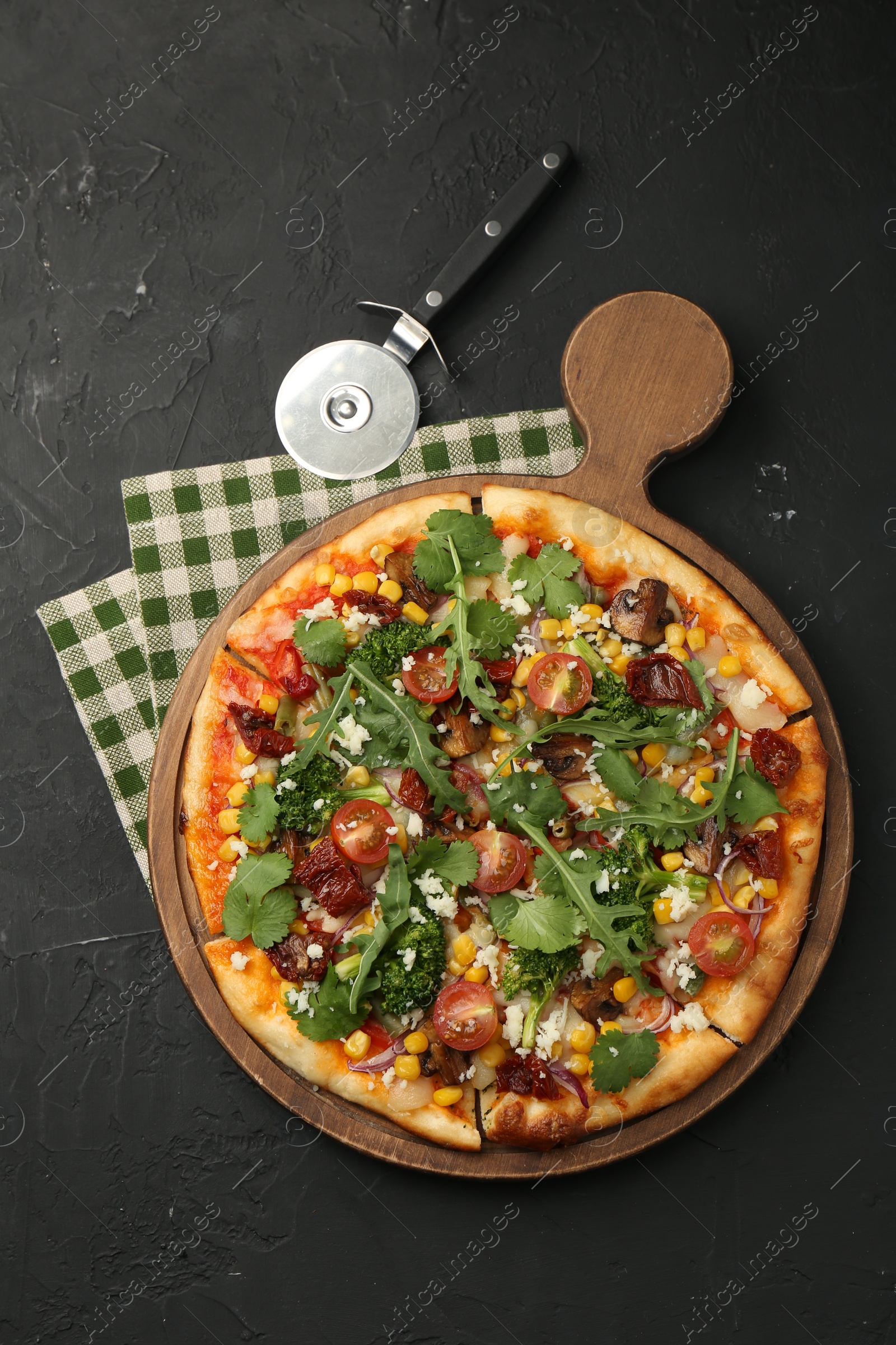 Photo of Delicious vegetarian pizza and cutter on black table, top view