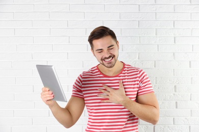 Photo of Man using tablet for video chat against brick wall