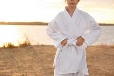 Photo of Cute little girl in kimono near river at sunset, closeup. Karate practicing