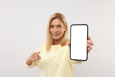 Photo of Happy woman holding smartphone and pointing at blank screen on white background, selective focus