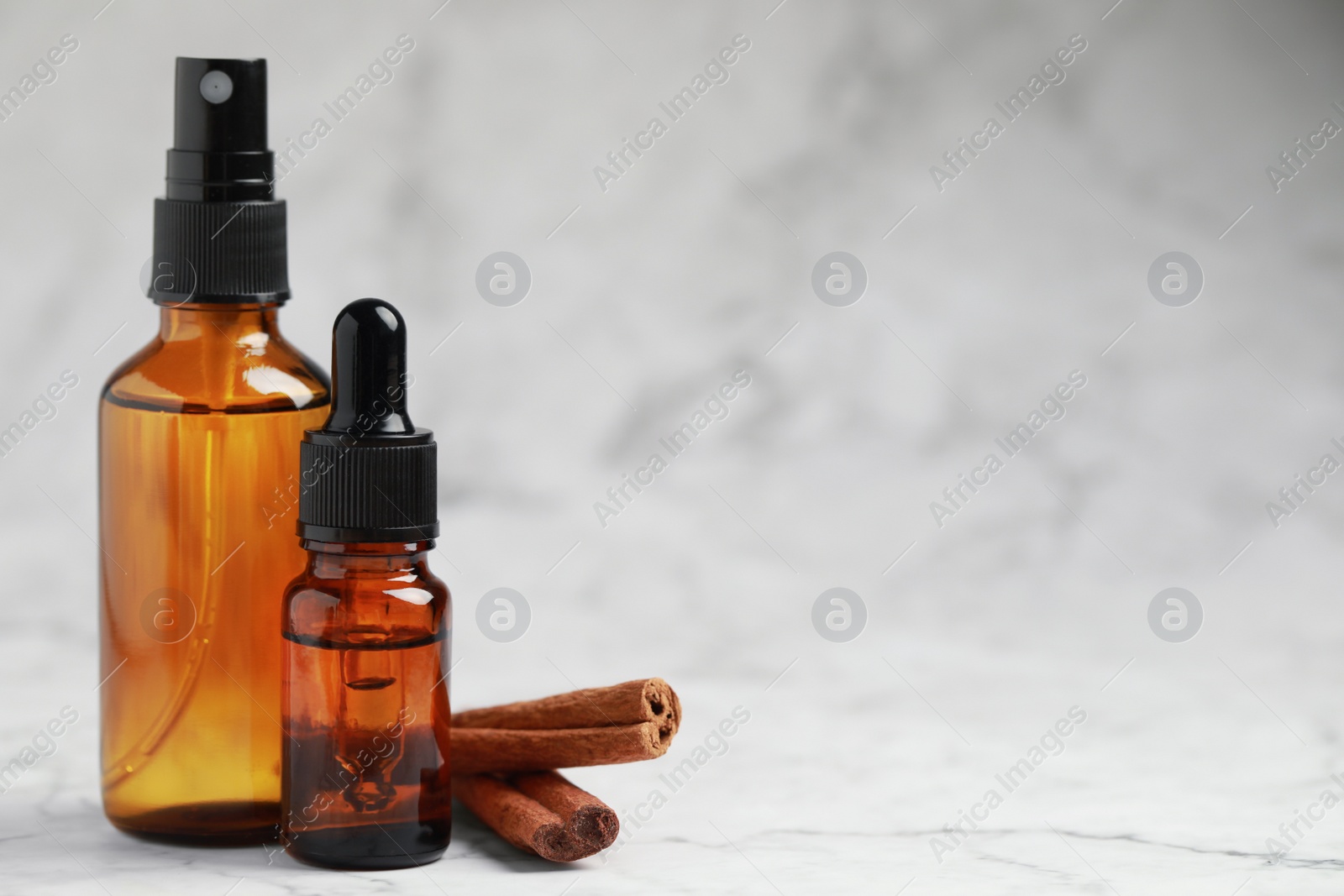 Photo of Bottles of organic cosmetic products and cinnamon sticks on grey marbled background, space for text