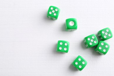 Many green game dices on white wooden table, flat lay. Space for text