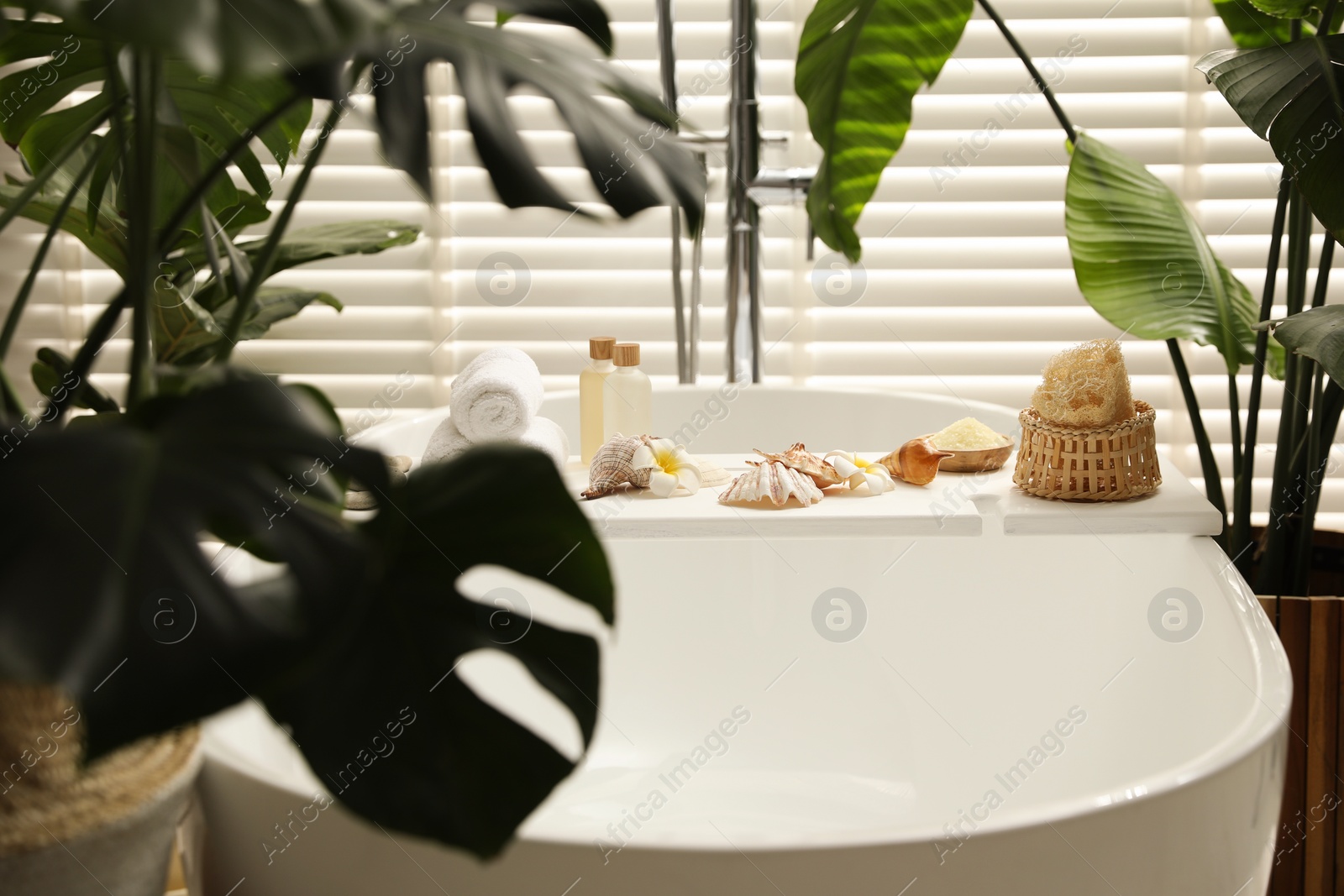 Photo of Bath tray with spa products, towels and shells on tub in bathroom