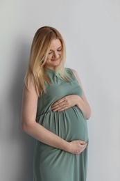 Young pregnant woman touching belly on light background