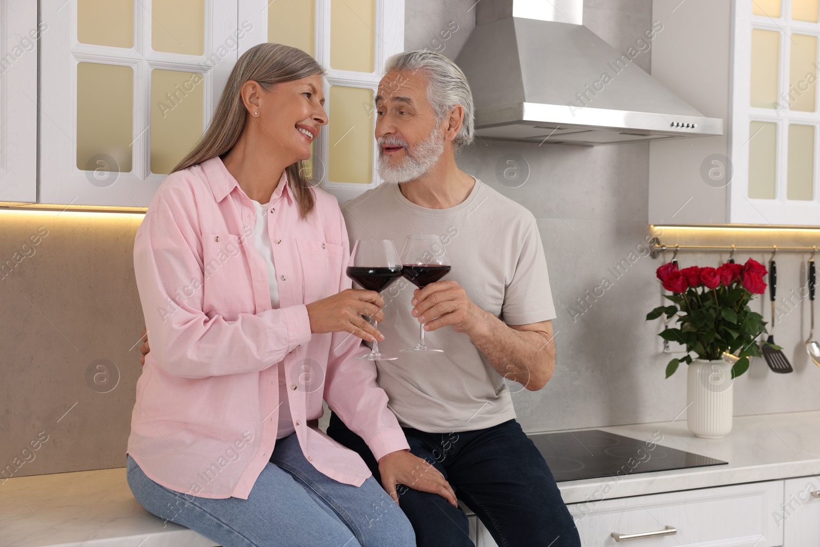 Photo of Happy affectionate senior couple with glasses of wine in kitchen